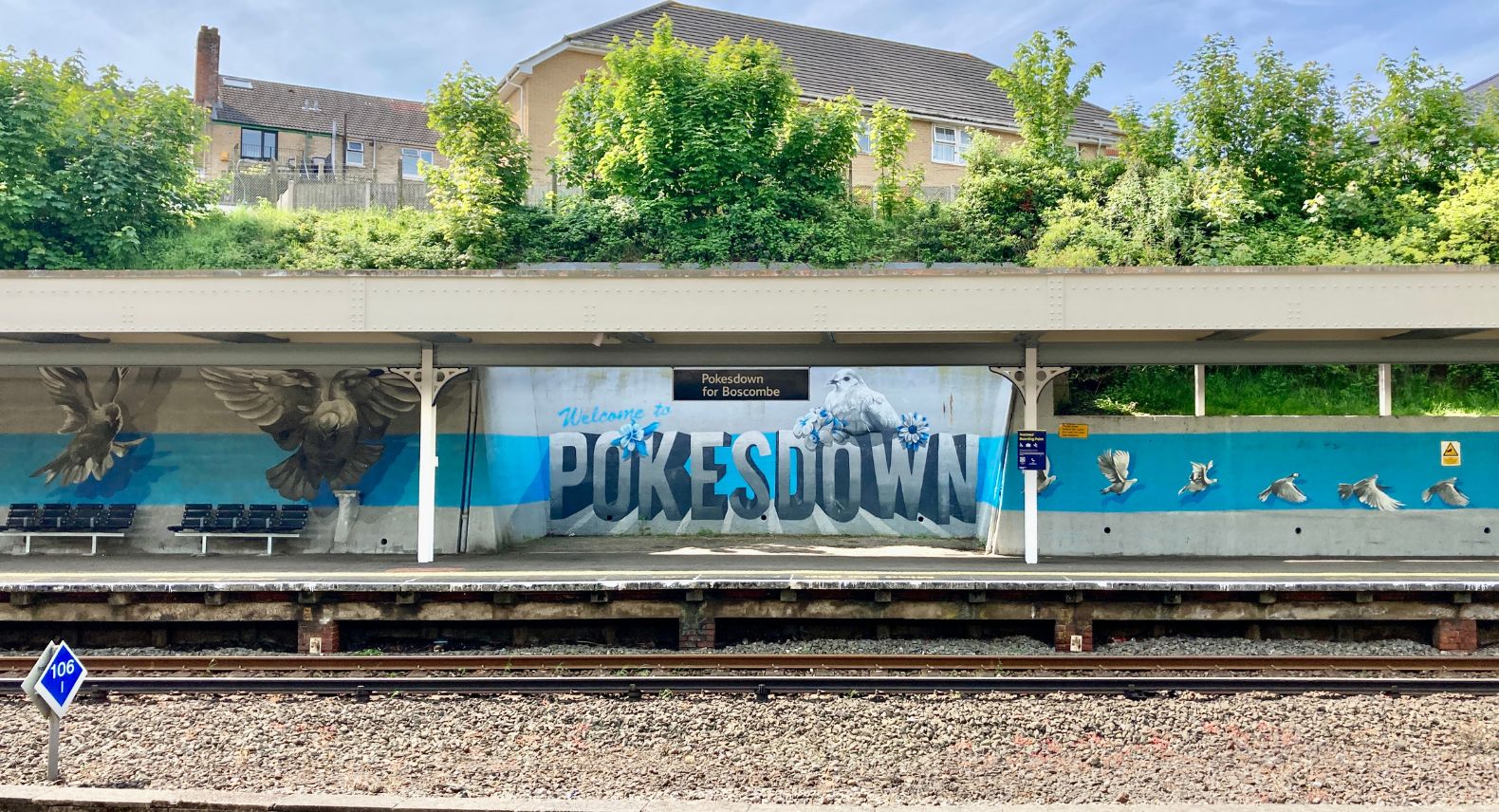 View across railway tracks to mural on opposite platform saying Welcome to Pokesdown with a bird painted resting on Pokesdown