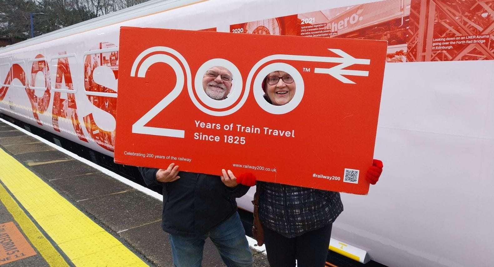 Couple looking through cut outs in a large placard saying Railway 200