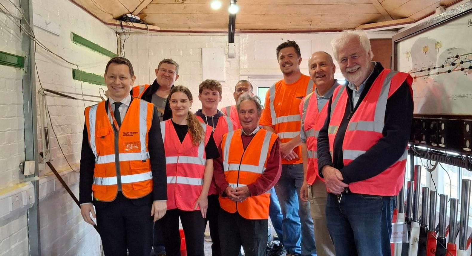 A group of nine people in high visibility tabards standing inside an old signal box