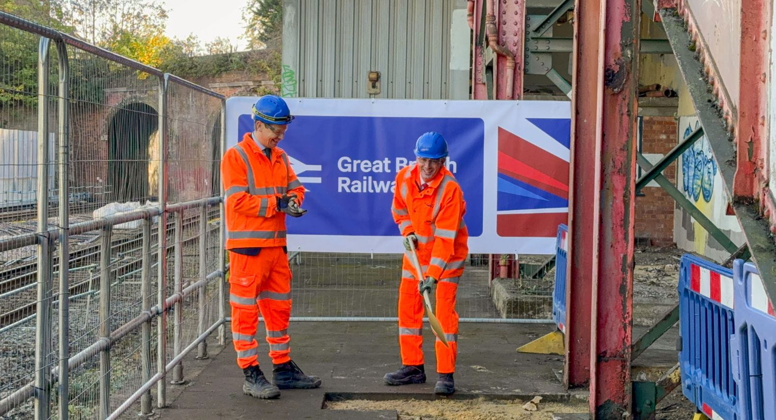 Two people in orange hi-viz standing in front of a Great British Rail sign