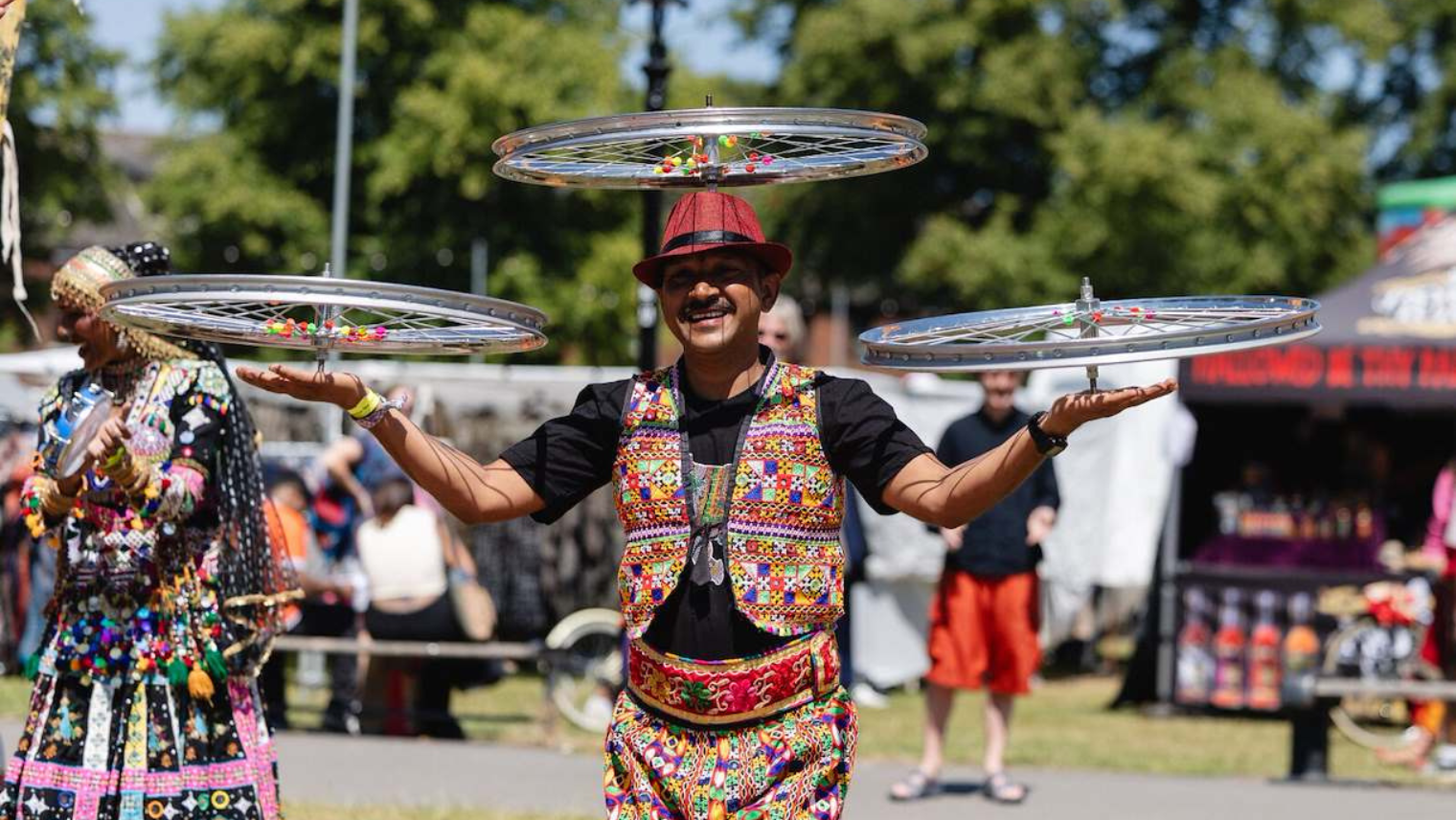 Performer balancing spinning bicycle wheels at an outdoor festival, wearing colourful traditional attire.