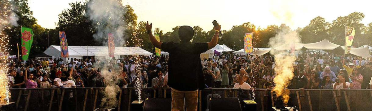 Singer on stage facing a cheering crowd with fireworks and smoke effects at sunset.