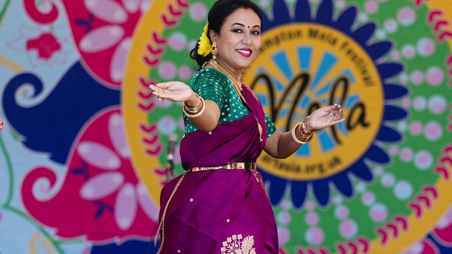 Dancer in vibrant sari performing traditional Indian dance against a colourful “Mela” festival backdrop