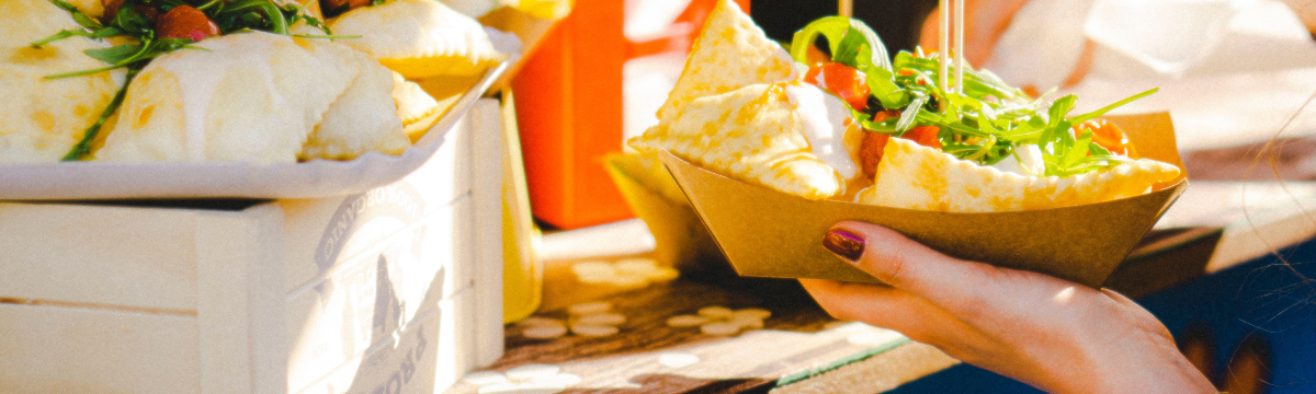 Fresh flatbread wraps filled with greens and tomatoes, served in paper trays at an outdoor market.