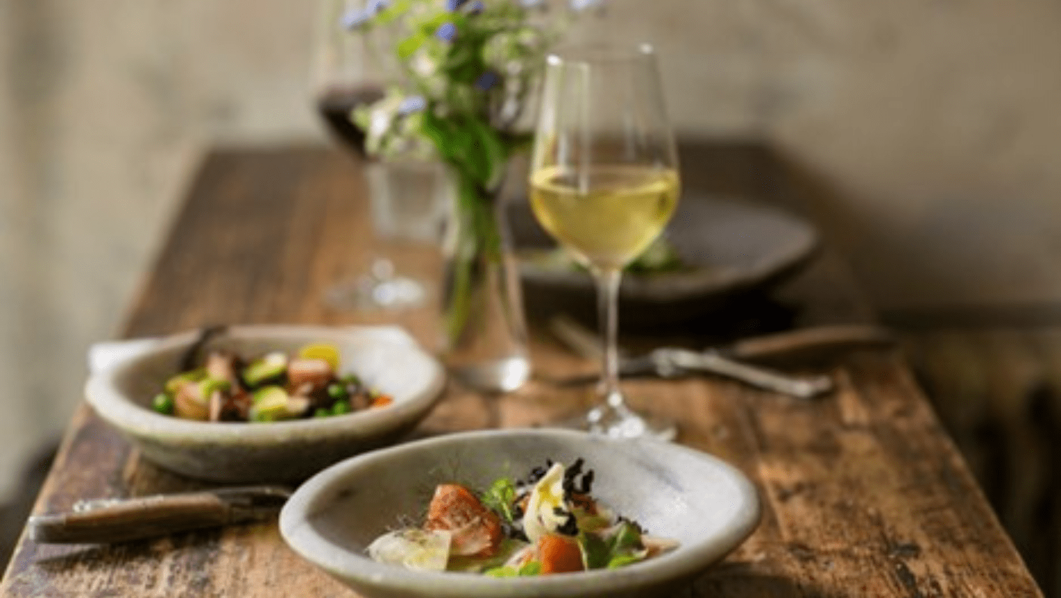 2 bowls of food and a glass of wine at a dinner table