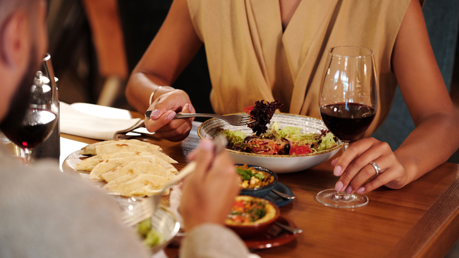 People dining with wine and salad at a restaurant table.