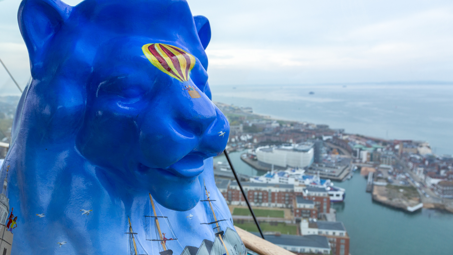 Blue lion sculpture overlooking Portsmouth harbour, with painted ships and a hot air balloon design on its head.