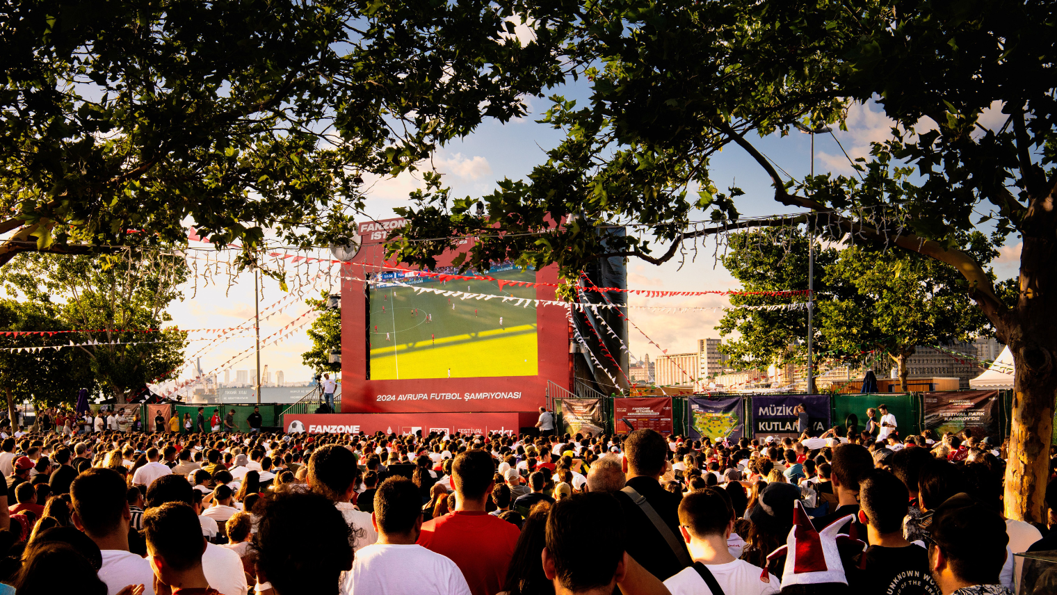 Crowd watching a football match on a big outdoor screen at a fan zone.