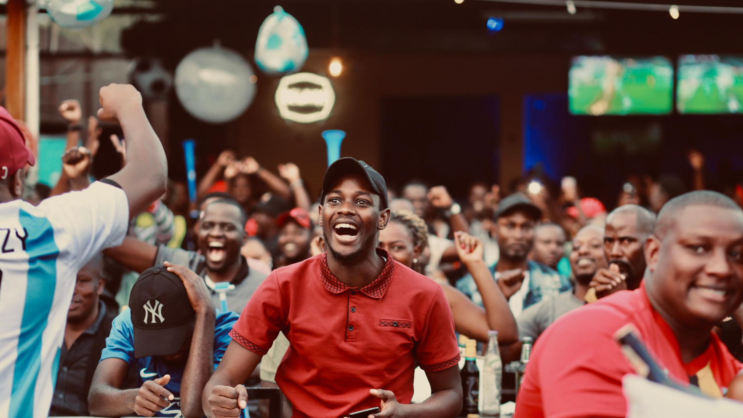 Excited crowd watching a football match indoors, cheering and celebrating together.