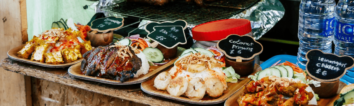 A street‑food counter showing dishes of tofu, prawns, and chicken beside a grill.