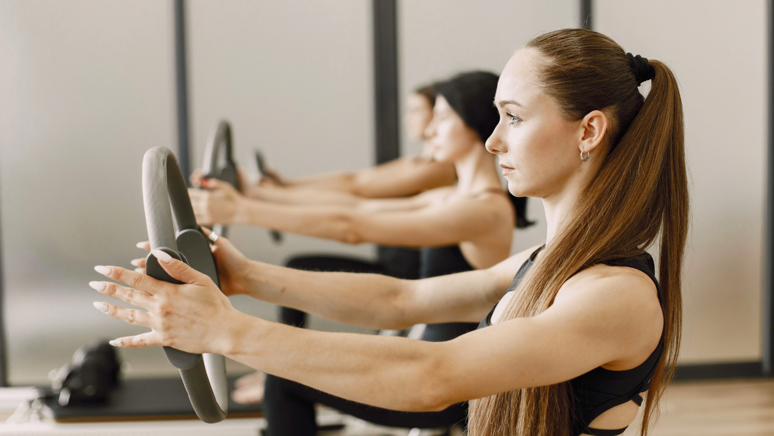 Three women practicing Pilates in a gym, focusing on their poses on exercise mats.