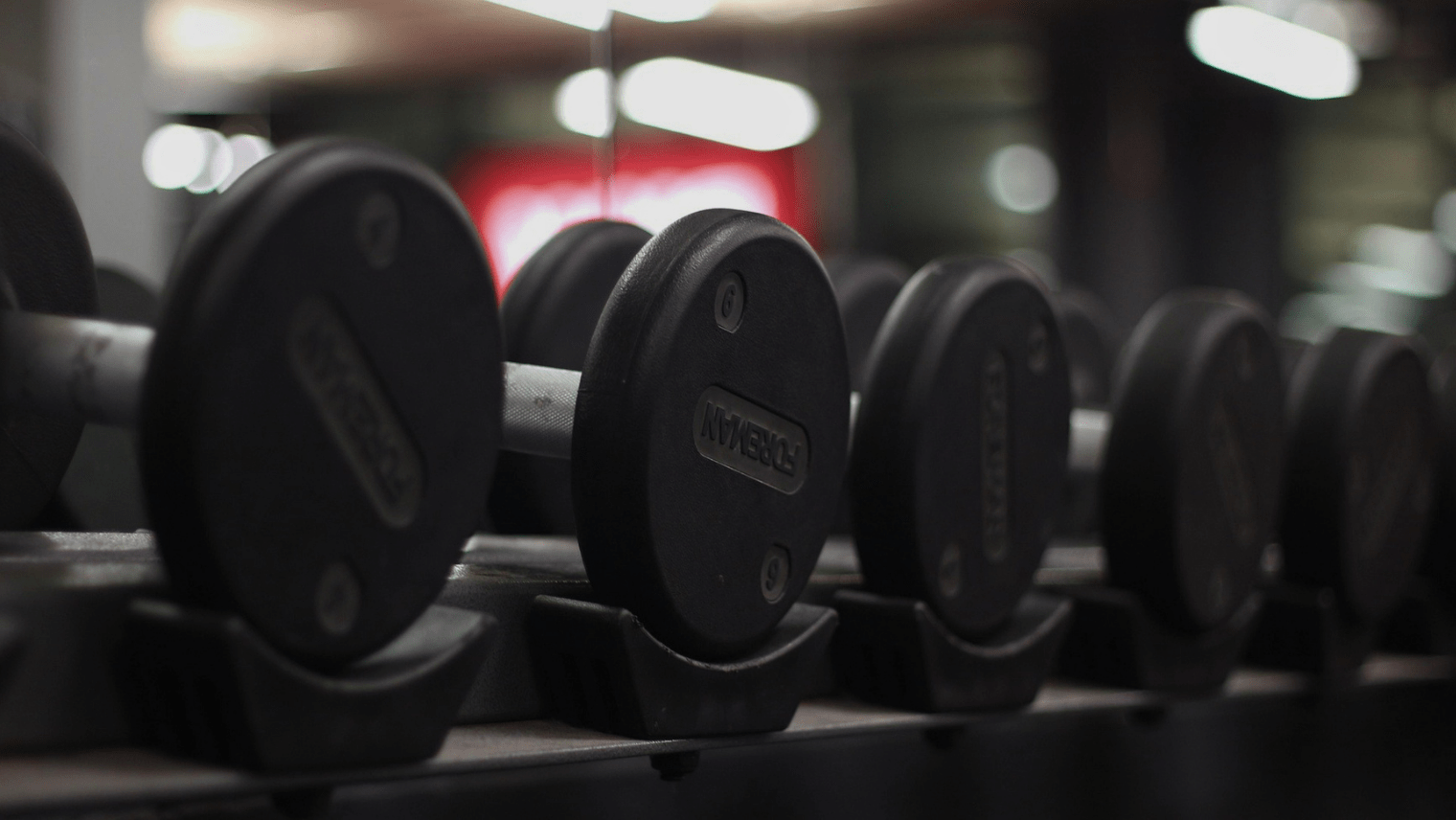  Several black dumbbells neatly lined up on a rack in a dimly lit fitness centre.