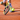  A tennis racket with a yellow and black frame hovers near a bouncing yellow ball on a reddish clay court, with a player’s shoes and white boundary lines visible.